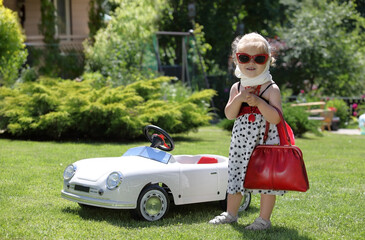 Funny little blonde girl  standing next to a toy car