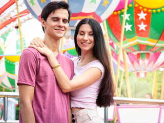Teenager sweet couple show love each other, young beautiful woman puts her arms around boyfriend's neck, lover hug each other, spend time together at theme park, lover hang out at amusement park