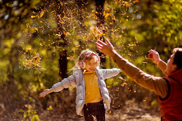 dad playing with daughter, throw dry yellow fallen leaves. walks in autumn Park.