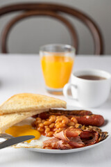 Typical English breakfast with fried eggs, sausages, bacon, beans, mushrooms, orange juice, toasts and coffee on the table. Copy space