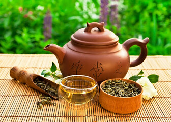 Obraz na płótnie Canvas Chinese tea cerermony in the garden. Clay teapot with glass cup, dry green tea and jasmine flower on a bamboo table.