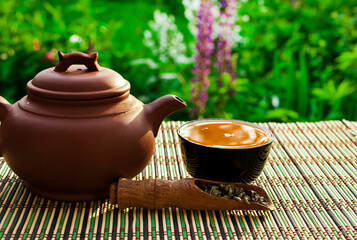 Chinese tea cerermony in the garden. Clay teapot with ceramic cup, dry green tea in wooden scoop on a bamboo table.