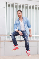 Casual guy sitting on a railing in the street