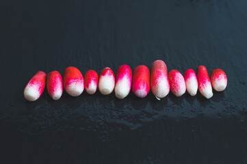 Line lined with fresh red peeled radish on a background of wet black stone