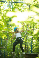 Extreme rope adventure in the forest - a little amazed girl standing on the rope bridge