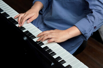 Female hands on the piano keys. Girl in a denim shirt. Plays the piano.