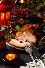 Roast pork neck in Christmas style. Dark navy blue background. Christmas accessories. Candles and lanterns in the background.