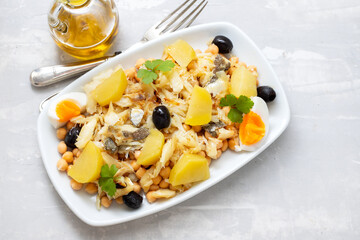 chick peas with cod fish, olives and boiled egg in white dish on ceramic background