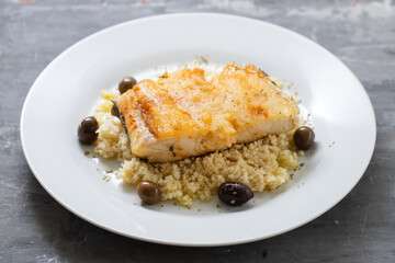 fried cod fish with cous cous and olives on white plate