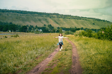 Fototapeta na wymiar A child a girl runs happily with her arms outstretched in rural summer nature against the backdrop of mountains and a lake