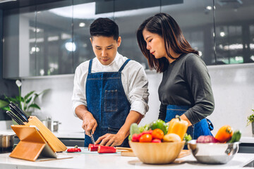 Young asian family couple having fun cooking together with fresh vegetable salad on table.Happy couple looking for recipe on Internet with tablet computer to prepare the yummy eating lunch in kitchen