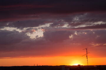 Natural sunset sunrise over the city and meadow. Bright dramatic sky and dark earth, beautiful clouds. Dawn Sunrise. The sun over the horizon, horizon. Warm colors. Beautiful sky.