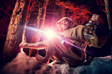 Medieval monk in canvas sackcloth robe with lattern resting on snow in dark forest and red light on...