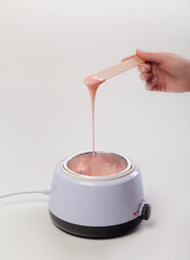 Wax melter on a white background. Salon equipment. Wooden spatula in female hands.