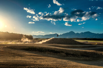 Motocross ride on dry dirt track full of dust. Late afternoon summer day. Alps mountains in the distance