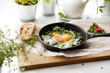 Eggs with green peas and spinach baked in a pan. Ready dish served in a hot pan. Suggestion of serving the dish. food background