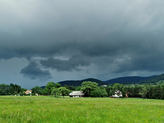 Obraz premium Poland Low Beskids Wysowa Zdroj. Storm clouds on the village. Green meadow with flowers.