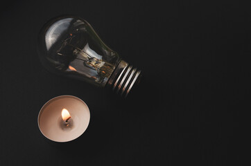 Electric lamp and candle on a dark background. Symbol of return to the past. Incandescent bulb and candle. Power cut or power outage. High electricity prices. Saving electricity.