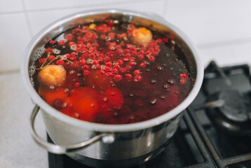Fresh fruits are boiled in boiling water in a metal pan on the stove. Delicious stewed apricot, apples, cherries, raspberries. Photography, concept.