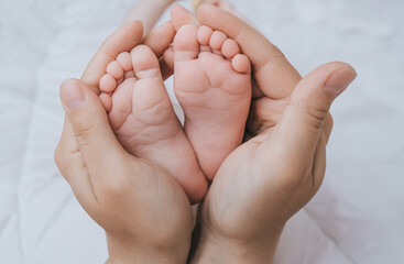 A caring and loving mother holds in her hands the legs and fingers of a small, newborn, sleeping baby on the bed close-up. Woman's happiness. Photography, concept.