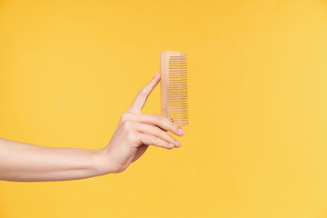 Side view of young well-groomed woman's hands keeping upright wooden while going to comb hair,...