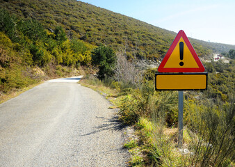 Mountain road with danger warning traffic sign. Triangular warning signal of undetermined danger for circulation on a lonely mountain county road