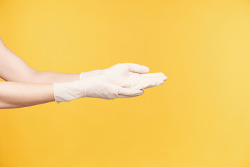Fototapeta na wymiar Side view of young woman's hands dressed in white rubber gloves keeping palms up while going to wash hands, being isolated against orange background