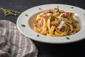 Close up pasta fettuccine with mushrooms, bacon, parmesan cheese in white plate with napkin on a dark wooden background. Selective focus 