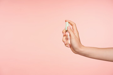 Side view of transparent spray bottle with liquid being held by young female's hand with nude...