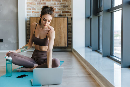 Image of pleased beautiful woman working with laptop while working out