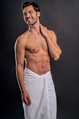 Fototapeta premium Handsome young bearded man isolated. Topless muscular man in towel is standing on grey background. Serious man looking away.