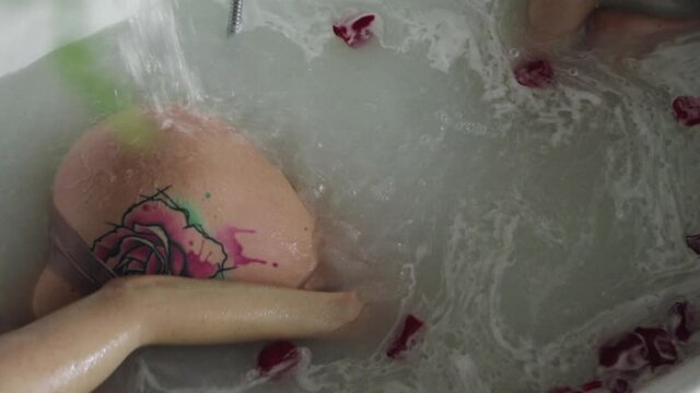 A young girl in lingerie bathes in a rose petal with a tattoo on her hip
