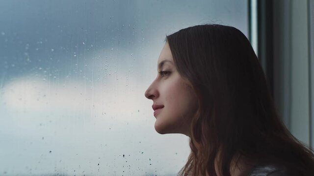 Tender woman enjoying rain out of window