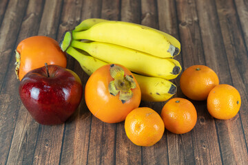 Fruits, bananas, clementines, persimmons and a red apple on a wooden table