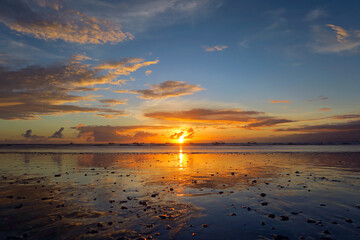 Beautiful Kuta beach sunset with clouds, rocks on sand and reflection, Bali island, Indonesia 