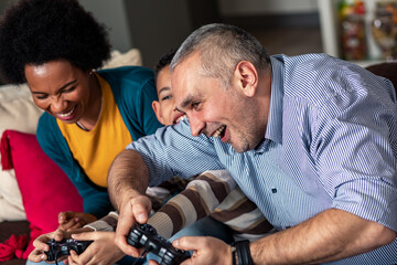 Smiling mixed race family enjoying time at home sitting on sofa in living room and playing video games.