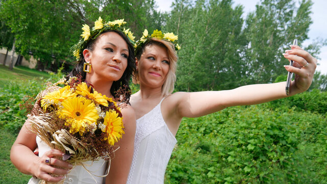Two bridesmaids taking selfies at a wedding. The bride takes a selfie with her sister. Two brides taking a photo at their wedding with phone.