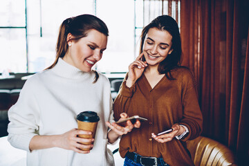 Cheerful female bloggers sharing information via bluetooth connection on smartphones, positive...