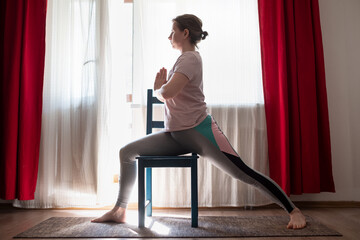 Woman doing virabhadrasana warrior pose at home using chair.