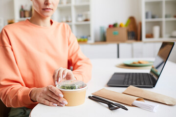 Close-up of woman sitting at the table and opening the box with food she ordering takeaway food