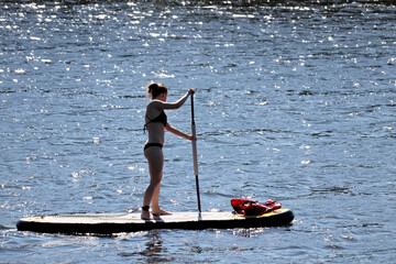 Sup surfing, standup paddleboarding in summer. Silhouette of girl in bikini standing with paddle on a board in glistening water