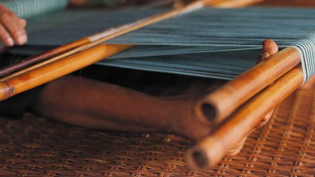 Laos, Pakse. Close up uf feet and hand of woman weaving in a traditional backstrap loom.
