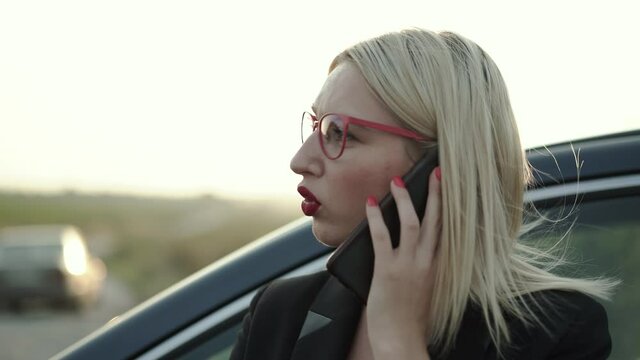 Blonde talking on the phone emotionally at car on highway at sunset