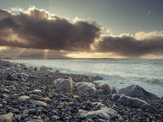 Obraz premium Rough stone beach at dusk, dark dramatic sky with sun light beams, Strandhill town, county Sligo, Ireland, Atlantci ocean. Nobody.