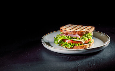 Sandwich with ham, cheese, tomatoes, lettuce, and toasted bread on dark background