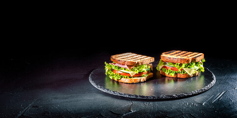 Sandwich with ham, cheese, tomatoes, lettuce, and toasted bread on dark background