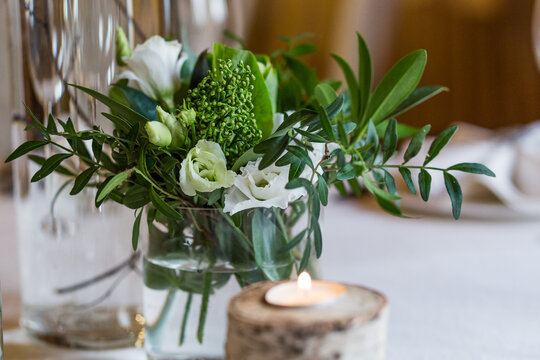 
Rustic-style floristics on a banquet table, white eustomas with saturated foliage in a glass vase on a banquet table, closeup shot.