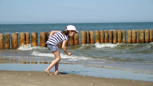 Little kid girl plays on Baltic sea beash shallow waterline summer rest during vacations