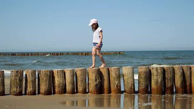 Little kid girl walks on wooden pier on Baltic sea beash near shallow waterline summer rest during vacations