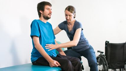 Physiotherapist exercising with disabled person using wheelchair on a therapy table.